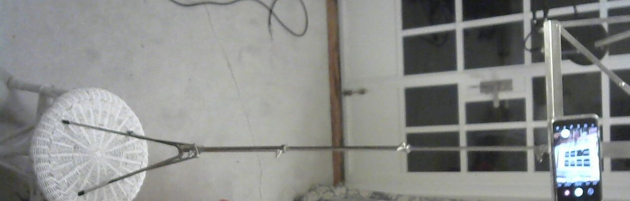 A phone, being used as a camera, sitting on a fully extended sheet
           music stand, sitting on a small chair/table